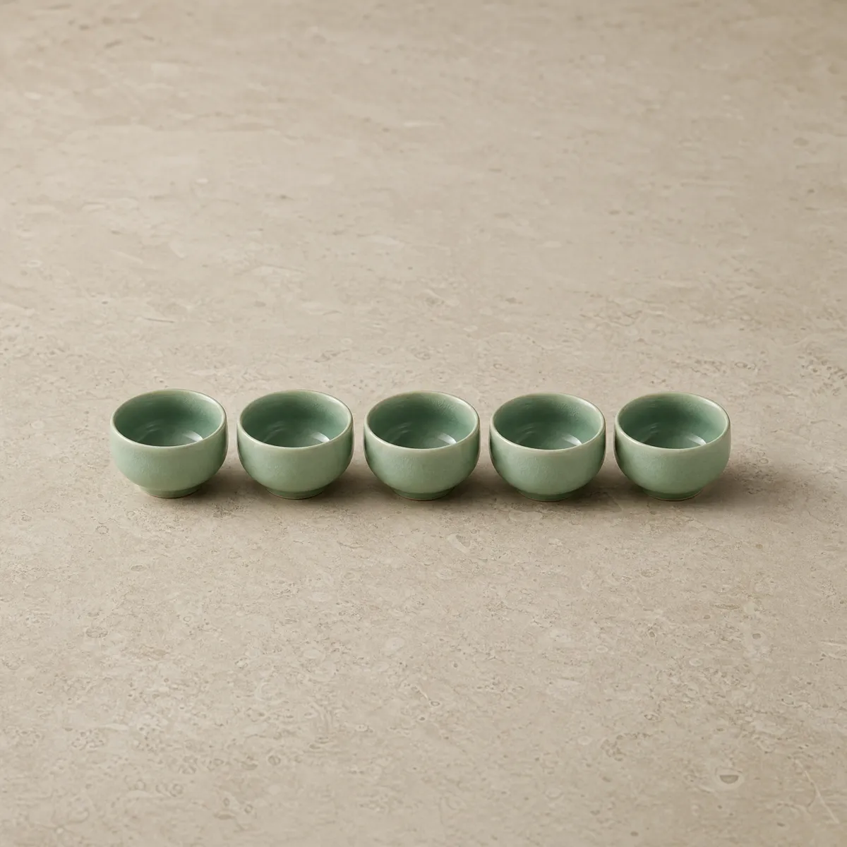 Five celadon teacups in a row on pale stone